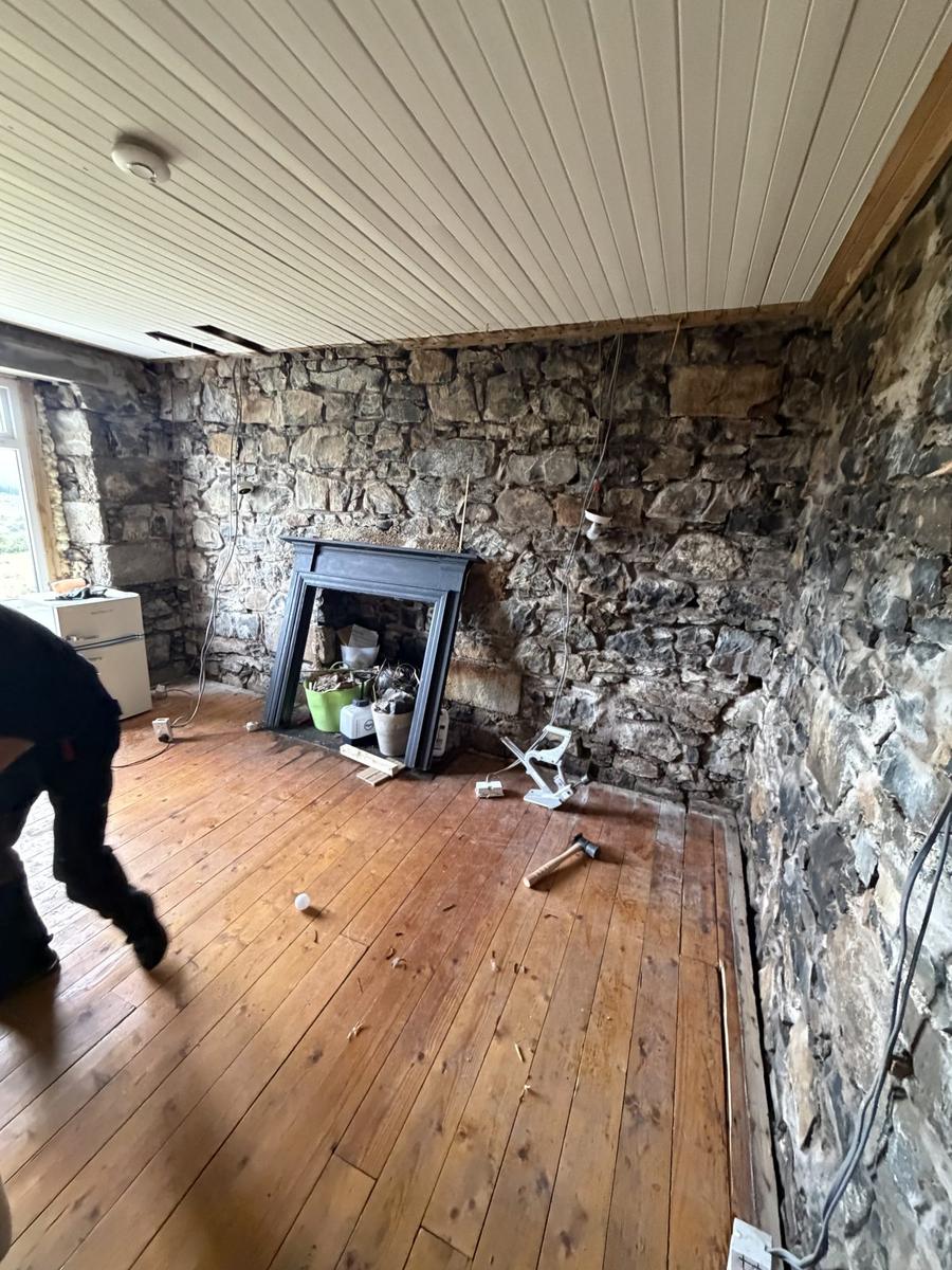 Bare rubble stone wall and cast iron fireplace before internal wall insulation, Skye